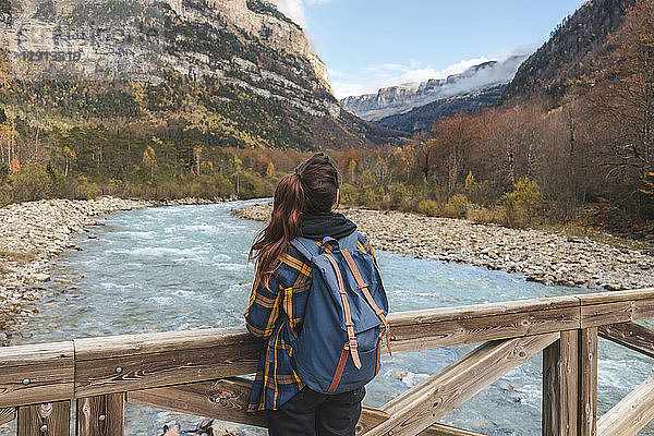 Spain  Ordesa y Monte Perdido National Park  back view of woman with backpack on wood bridge