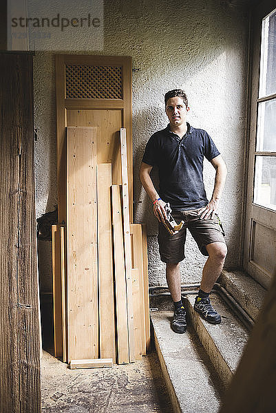 Portrait of smiling carpenter standing in his workshop holding plane