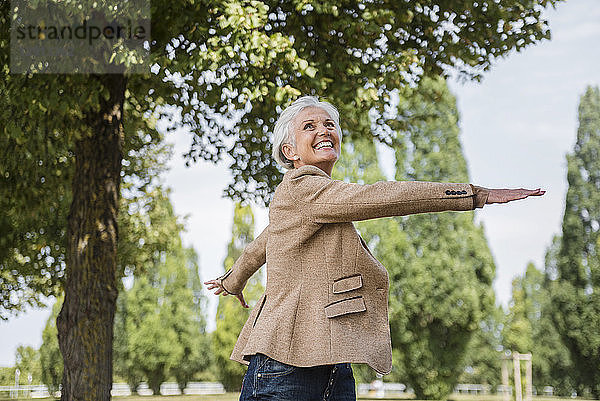 Happy senior woman with outstretched arms in a park