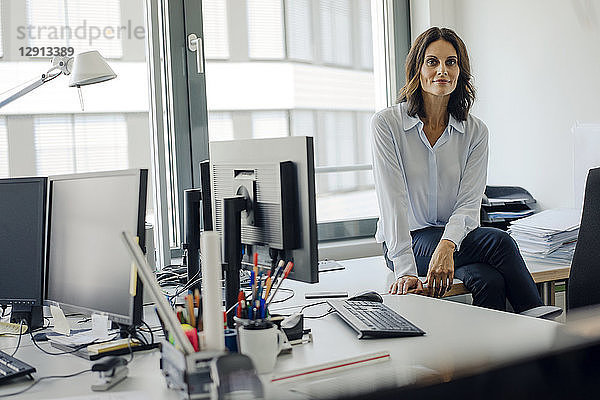 Mature businesswoman sitting o desk in office  smiling
