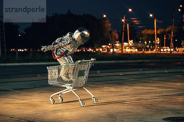 Spaceman in the city at night on parking lot inside shopping cart
