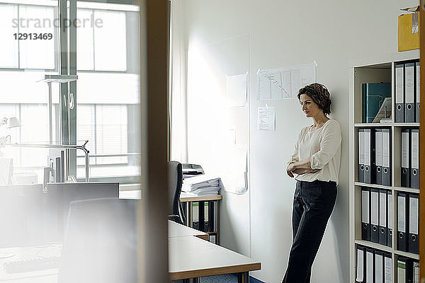 Businesswoman leaning against wall in office  with arms crossed