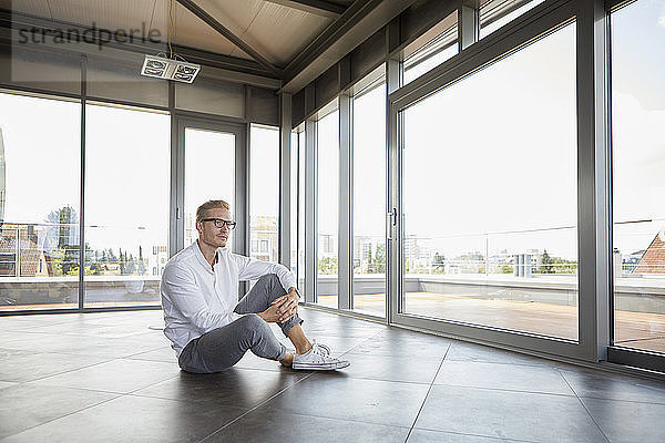 Businessman sitting in empty room looking out of panorama window