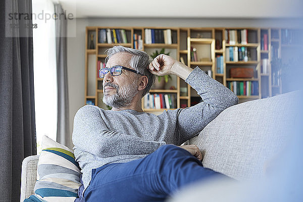 Mature man relaxing on couch at home looking out of window