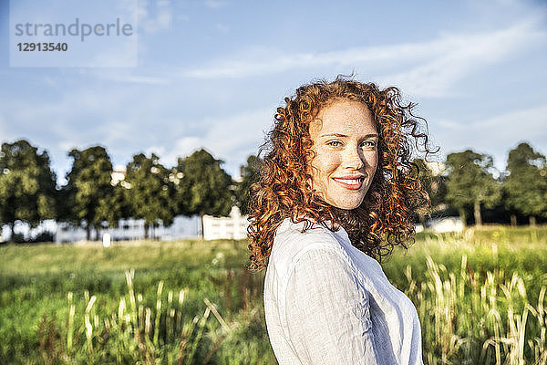 Germany  Cologne  portrait of smiling young woman with curly red hair in nature