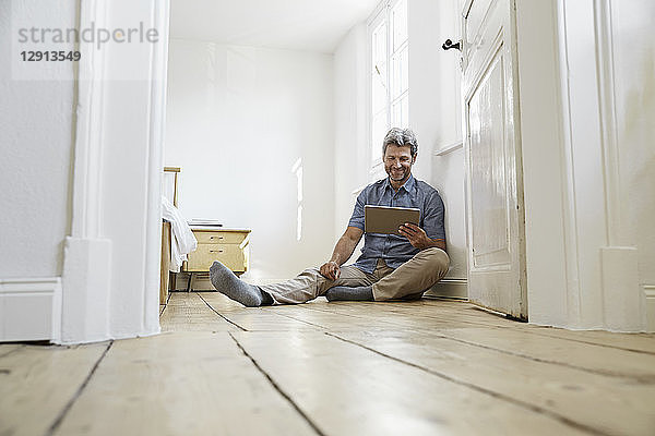 Marture man sitting on floor of his bedrom  using digital tablet