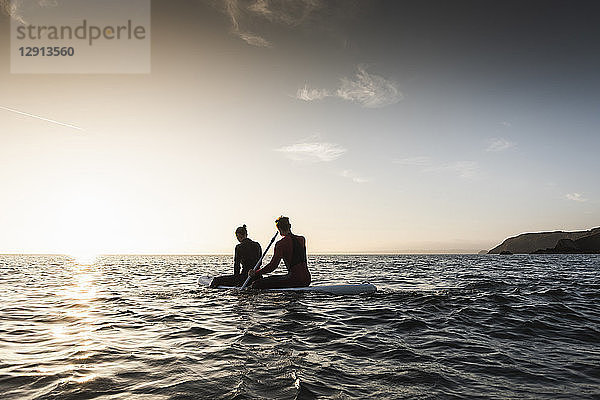 Couple on paddling on paddleboard at sunset on the sea
