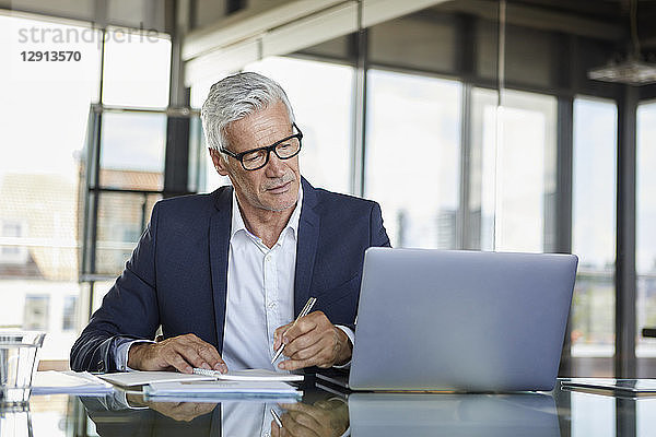 Businessman working at laptop  taking notes in notebook