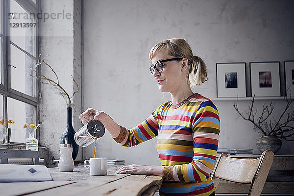 Woman pouring coffee in a mug at desk in a loft