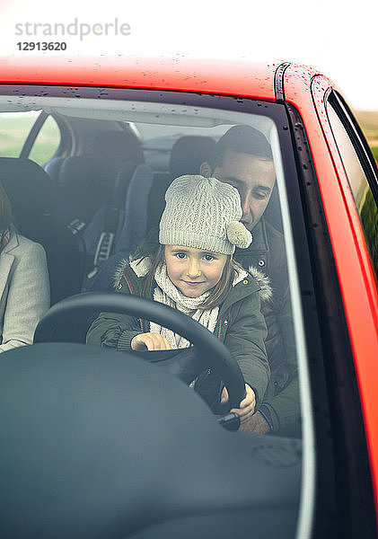 Little girl with wool cap driving car sitting on father's lap