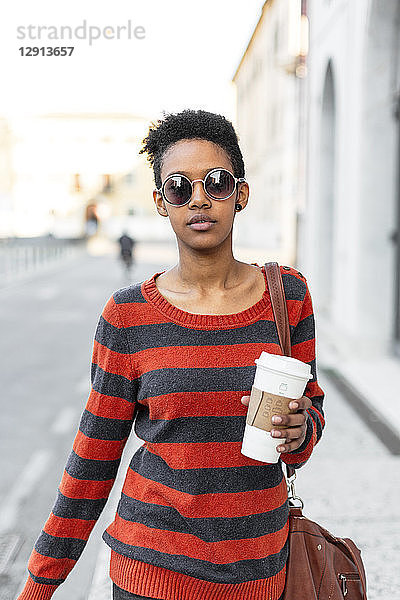 Portrait of young woman with coffee to go wearing sunglasses and striped pullover