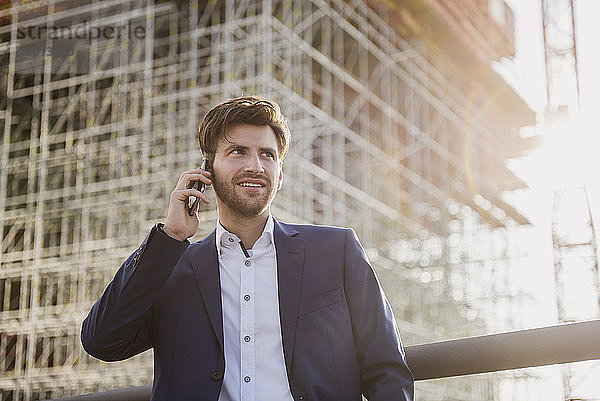 Businessman standing on bridge in front of construction site talking on cell phone