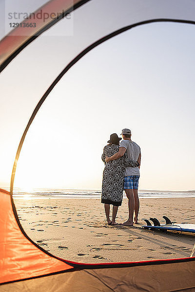 Romantic couple camping on the beach  embracing at sunset