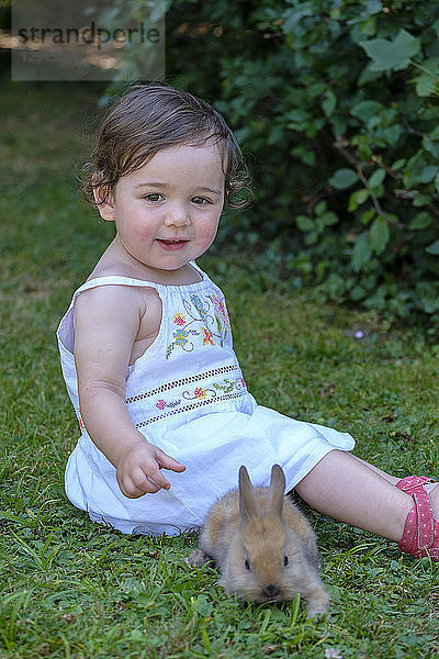 Portrait of content baby girl sittting on a meadow with young bunny