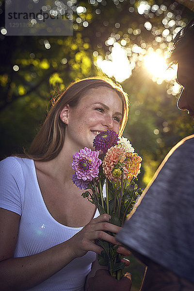 Young man meeting his girlfriend in a park  gifting her with flowers