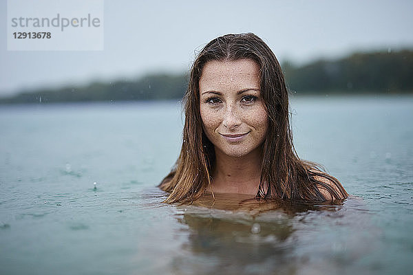 Portrait of freckled young woman bathing in lake on rainy day