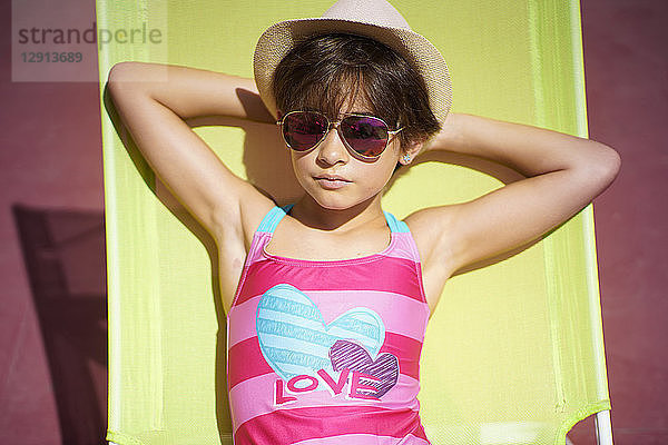 Young girl wearing swimwear  sunglasses and a sun hat  sitting in sun lounger