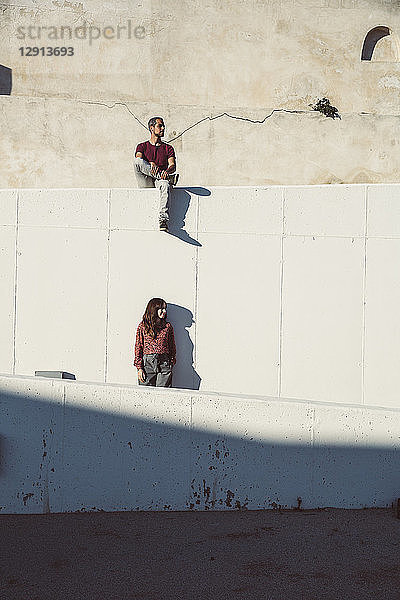 Man and woman standing and sitting on different levels of a wall