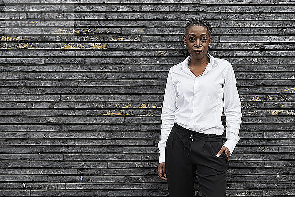 Portrait of smart businesswoman wearing white shirt and black trousers leaning against wall