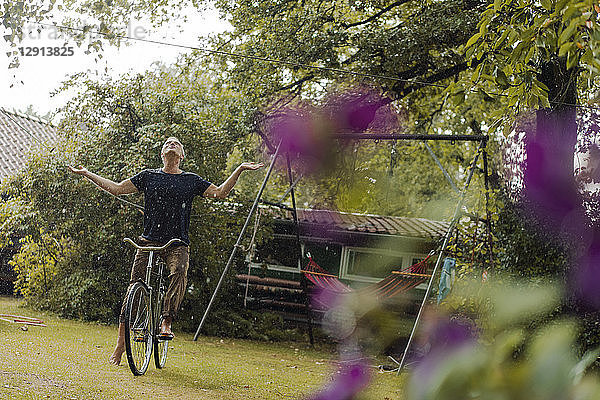 Mature man with bicycle enjoying summer rain in garden