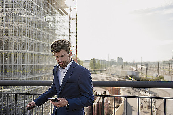 Businessman standing on bridge in the city using cell phone