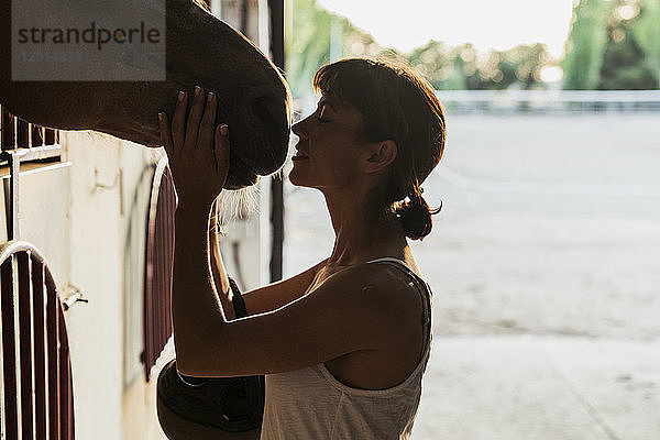 Smiling woman stroking horse in stable