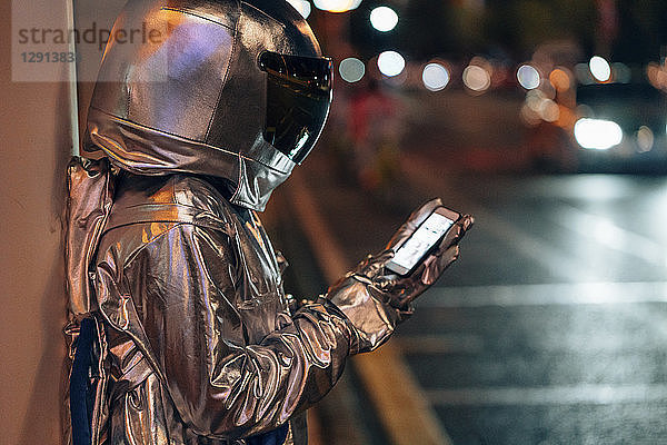 Spaceman at a city street at night using cell phone