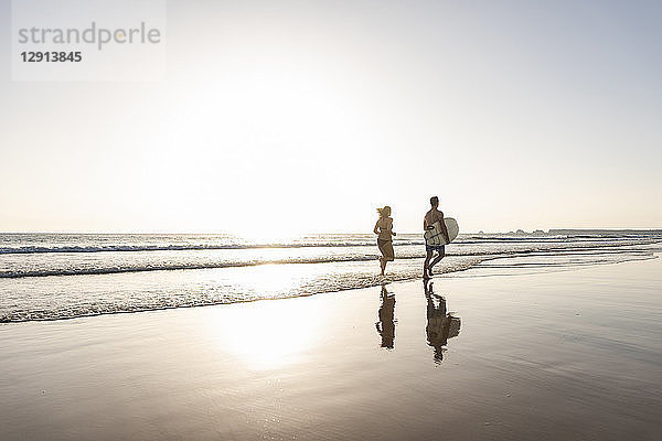 Young couple running on beach  carrying surfboard