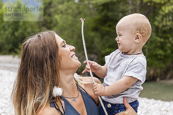 Smiling mother with baby boy holding a stick in the nature