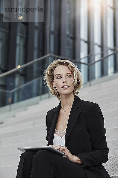 Portrait of blond businesswoman with tablet sitting on stairs outdoors