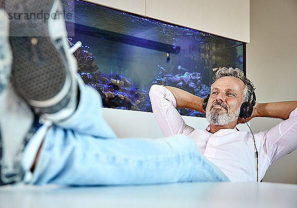 Relaxed mature man listening to music with headphones in front of aquarium