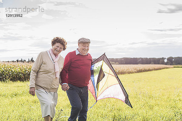 Happy senior couple walking with kite in rural landscape