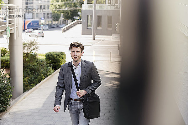 Smiling businessman with crossbody bag in the city on the move