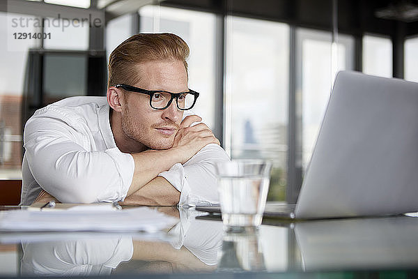 Businessman leaning on desk in office with laptop