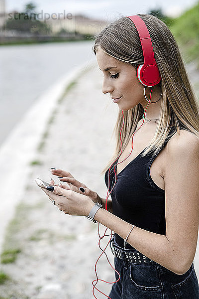 Teenage girl at the riverside wearing headphones using cell phone