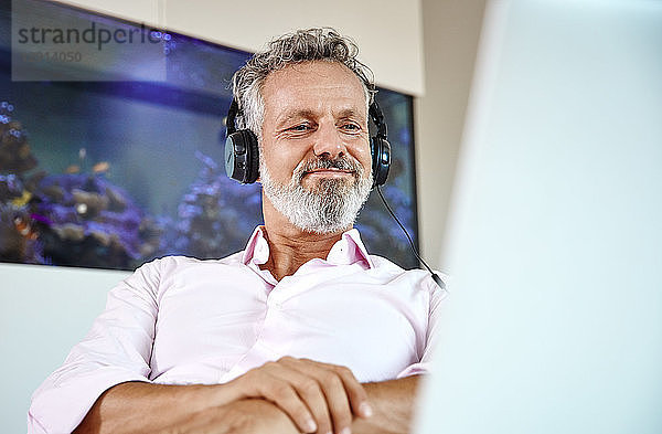 Businessman with headphones using laptop at desk in front of aquarium