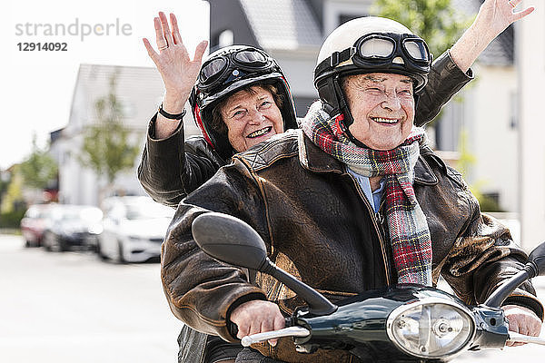 Happy senior couple having fun  riding motor scooter and waving
