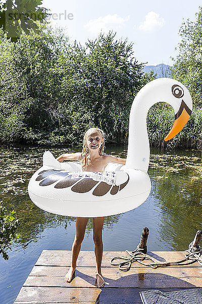 Happy girl standing on jetty at a pond with inflatable pool toy in swan shape