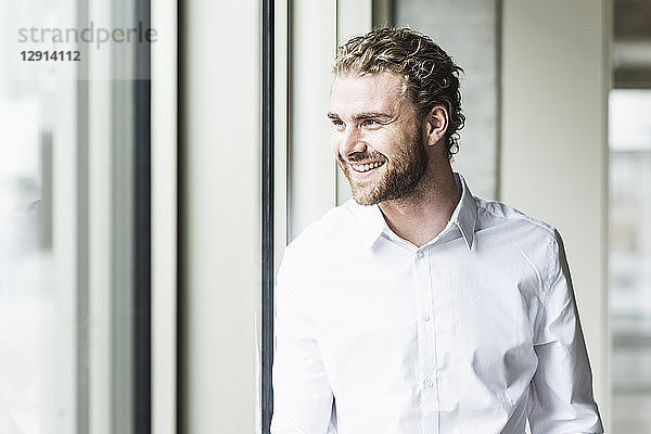 Smiling young businessman looking out of window in office
