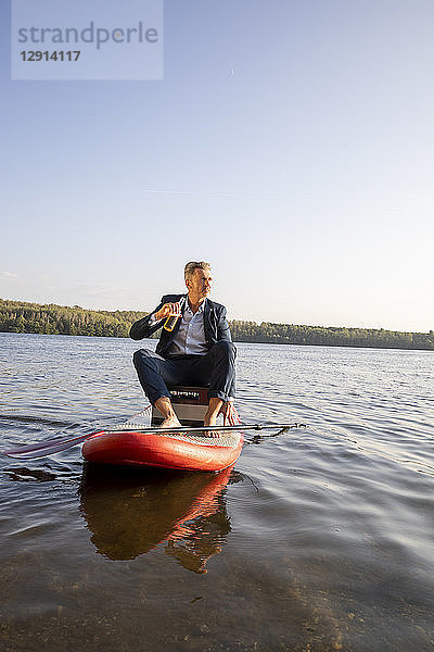 Businessman relaxing with drink on paddleboard on a lake