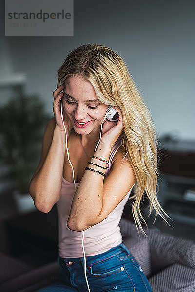 Smiling young woman listening to music with headphones at home