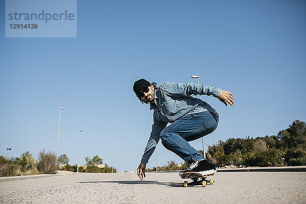 Trendy man in denim and cap skateboarding
