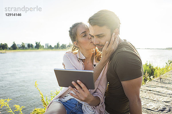 Couple kissing at the riverside in summer holding tablet