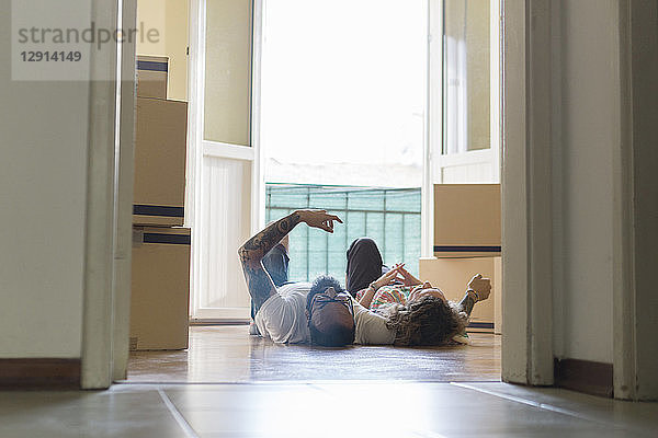 Couple lying side by side on the floor of new home in front of open balcony door