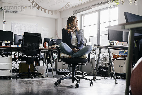 Businesswoman sitting cross-legged on an office chair