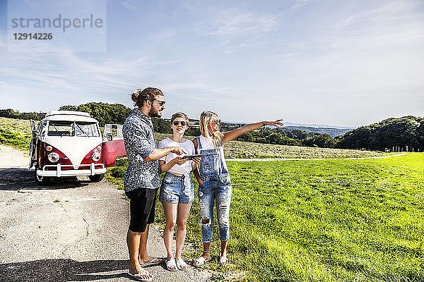 Friends with tablet outside van in rural landscape