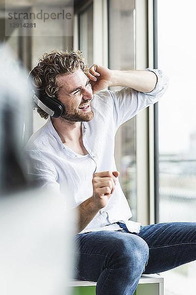 Happy casual young man listening to music with headphones at the window