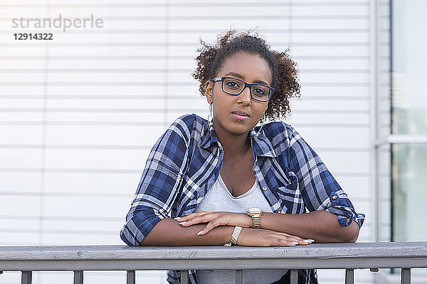 Portrait of young woman wearing glasses leaning on railing