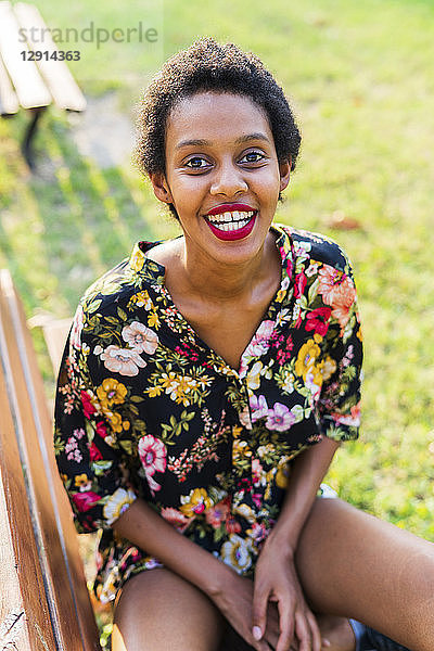 Portrait of laughing young woman sitting on bench in a park