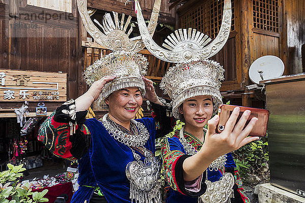 China  Guizhou  two Miao women wearing traditional dresses and headdresses taking a selfie with smartphone
